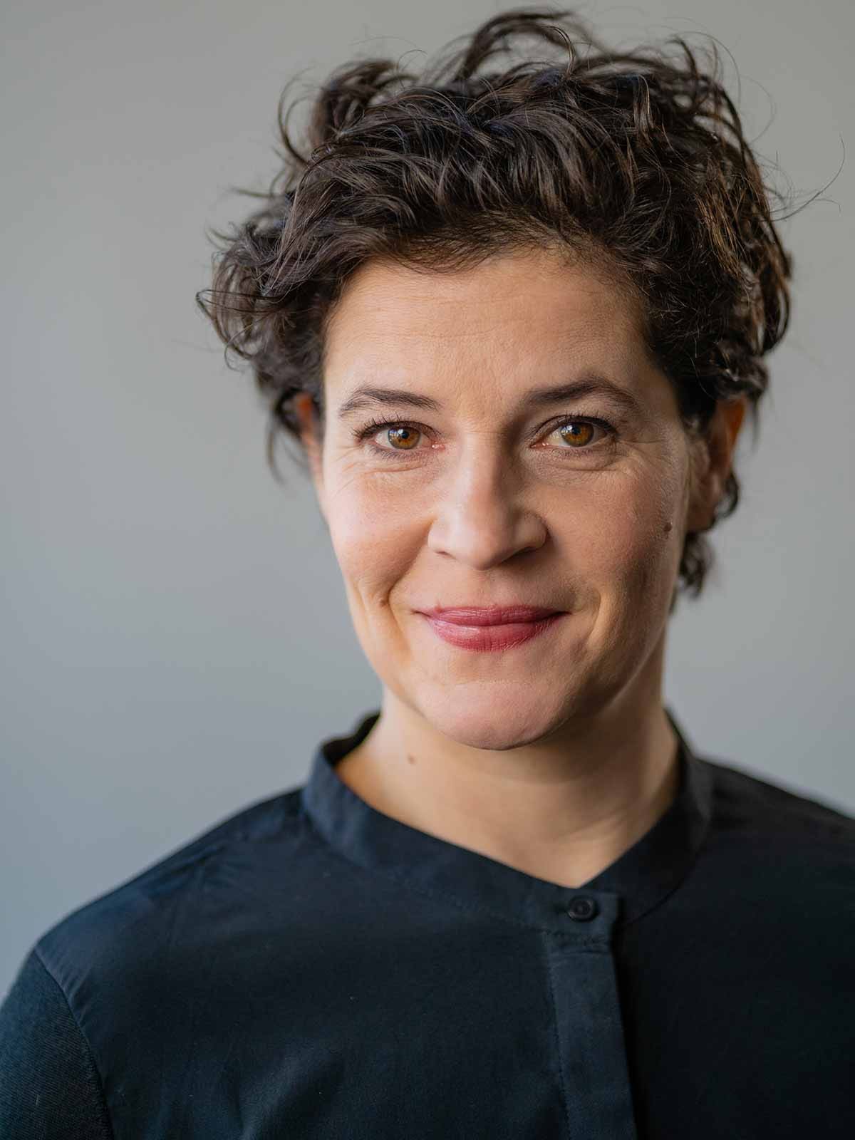 Cathérine Seifert im dunklen Hemd, frontal porträtiert, mit leichtem Lächeln.