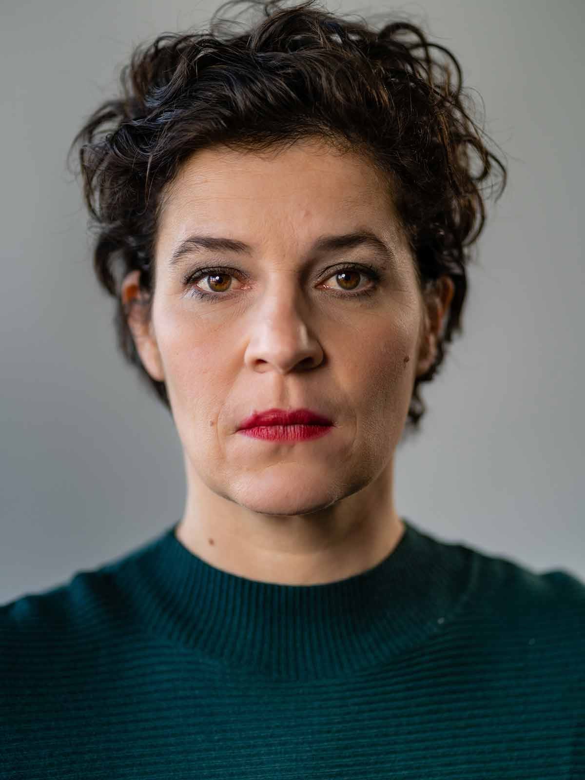 Cathérine Seifert im dunkelgrünen Rollkragenpullover, frontal porträtiert, mit ernstem, direktem Blick.